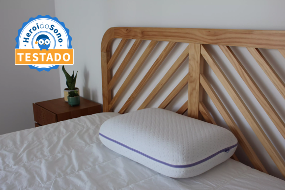 Almofada branca de espuma viscoelástica colocada sobre uma cama com cabeceira em madeira clara, com uma mesa de cabeceira em madeira escura com uma planta.